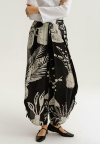 Černé široké kalhoty s vzory, které mají bílé květinové a vázičkové motivy, vyrobené z lehkého materiálu s elastickým pasem a stahovací šňůrkou.