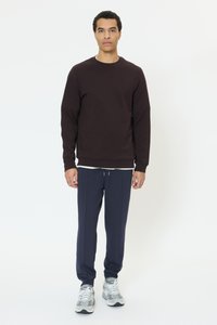 Ciemnobrązowa bluza z okrągłym dekoltem, zestawiona z granatowymi spodenkami dresowymi. Szare sneakersy z białymi akcentami. Prosty, sportowy design.