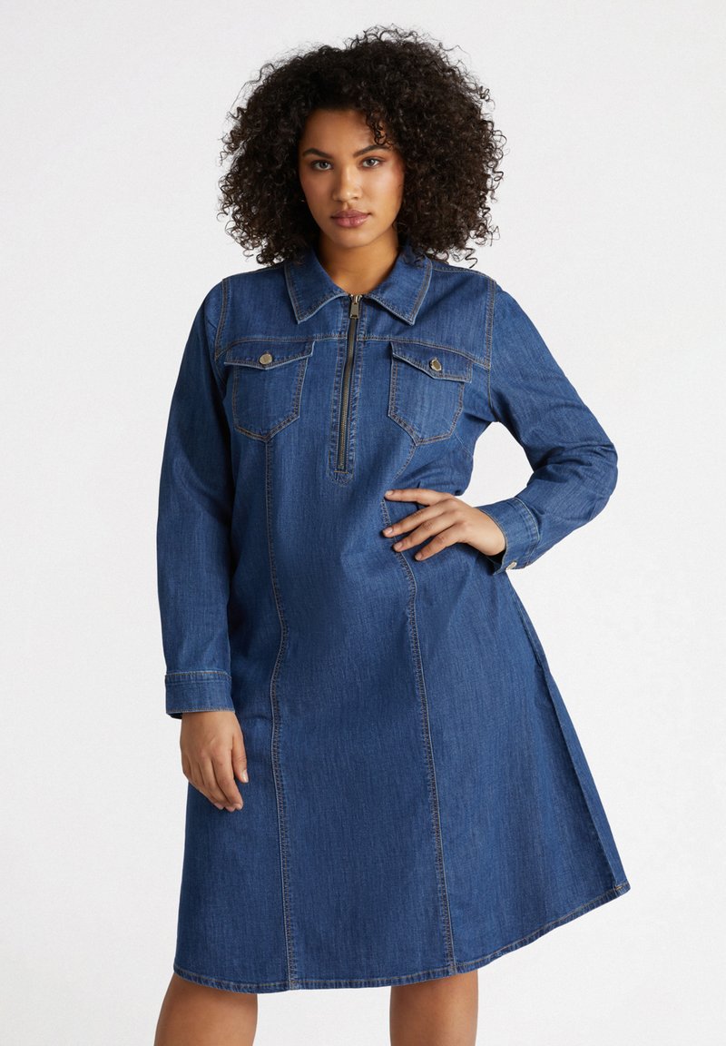 Denim mekko pitkähihaisilla, kauluksella ja vetskarihaalla. Varustettu kahdella rintataskulla, sivuhalkioilla ja jämäkällä muotoilulla. Tumma sininen väri.