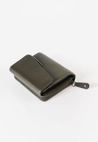 Portafoglio in pelle verde scuro con superficie testurizzata, chiusura a zip e pattina liscia a contrasto. Presenta un anello per il fissaggio.