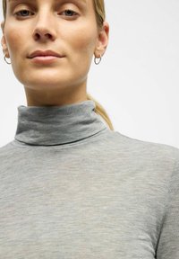 Sivi pulover s visokim ovratnikom napravljen od mekog, laganog materijala. Ima visoki ovratnik i gladak, blago teksturiran površinski sloj.