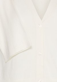 Cardigan ivoire avec col en V et manches courtes, présentant une texture côtelée et cinq boutons en perle sur le devant.