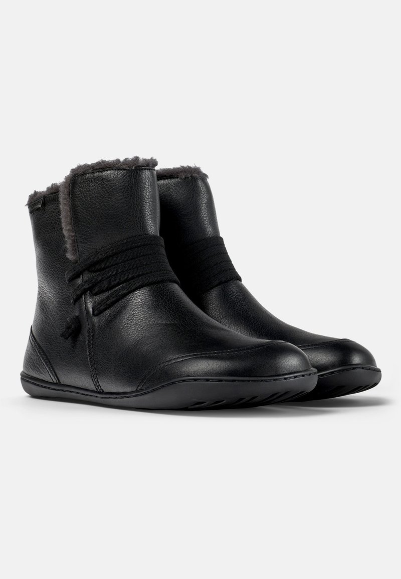 Svarta läderankelboots med en mjuk, grå pälsfoder upptill, som har elastiska band för stängning och en flexibel sula.