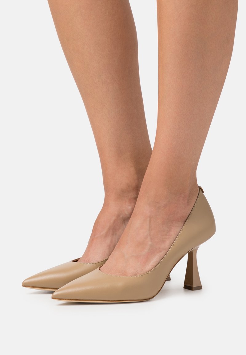 Escarpins en cuir beige avec un bout pointu et un petit talon carré. Texture lisse et design minimal avec une silhouette élégante.