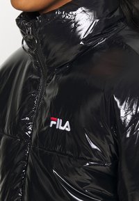 Giacca a vento nera lucida con collo alto, chiusura con zip e logo FILA ricamato in rosso e bianco sul petto.