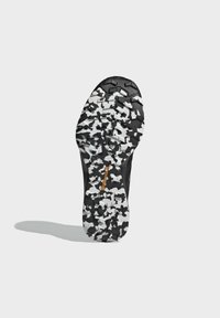 Sole di scarpe sportive nere caratterizzata da un design robusto con un motivo di camuffamento bianco e nero, scanalature profonde e un logo di marca ben visibile.
