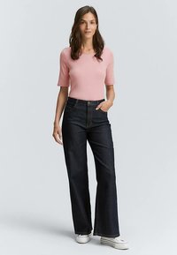 Ljusrosa figursydd topp med korta ärmar kombinerad med mörka högmidjade jeans med utsvängda ben. Vita sneakers fulländar outfiten.