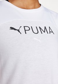 Camiseta de manga corta blanca con el logo de PUMA en negro. Cuenta con una tela texturizada, mangas raglán y un cuello suave para mayor comodidad.