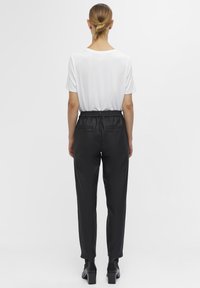 Zwarte broek met elastische tailleband en een gladde afwerking, gecombineerd met een effen wit shirt met korte mouwen, gezien van achteren.