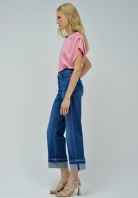 Top rosa de manga corta con hombros fruncidos, combinado con vaqueros anchos de talle alto en azul con dobladillos en el bajo, y tacones nude con tiras.