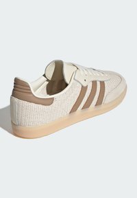 Baskets avec une tige en maille crème, des accents en cuir beige et trois rayures horizontales marron. Elles comportent une semelle en caoutchouc et un design à lacets.