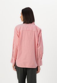Camicia a maniche lunghe a strisce rosse e bianche con colletto bottonato, polsini larghi, vestibilità rilassata e orlo curvo, realizzata in tessuto leggero.