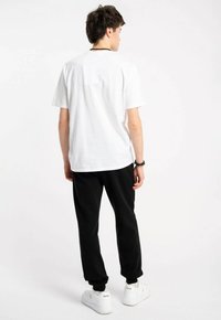 Biała bawełniana koszulka o luźnym kroju, zestawiona z czarnymi dresami. Białe sneakersy dopełniają stylizację. Styl jest casualowy i wygodny.