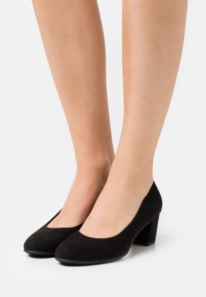 Chaussures à talon bloc en daim noir avec un bout arrondi et un design légèrement découpé. Le talon mesure environ 5 cm de hauteur.