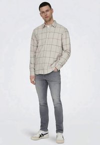 Cămașă bej deschis cu carouri, cu design cu nasturi, asortată cu blugi gri și adidași albi cu accente negre.