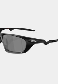 Lunettes de soleil noires avec des verres gris, présentant un design enveloppant et des bords angulaires. Comprend un logo ovale au niveau de la branche et des branches texturées.