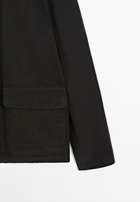 Black jacket with a zip closure, large front pocket, and long sleeves. Smooth texture and minimal design.