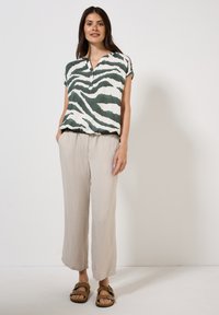Blusa de manga corta a rayas verdes y blancas con color de pico, combinada con pantalones de lino beige claros y sandalias marrones con tiras.