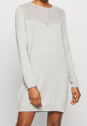 Langärmeliges, hellgraues Strickkleid mit Chevron-Spitzenmuster über der Brust, auf einer stehenden Person in mittlerer Oberschenkellänge getragen.