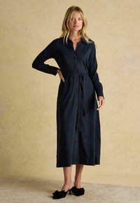 Dlhé rukávy, námornícky modré šaty s leopardím vzorom, zapínanie na gombíky a zaviazaný pás. Hladká látka a dĺžka pod kolená. Nosené s čiernymi topánkami zvýraznenými mašlou.