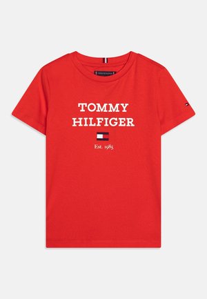 Camiseta roja de manga corta con texto "Tommy Hilfiger", pequeño logotipo de bandera y "Est. 1985" impreso en blanco en la parte delantera.