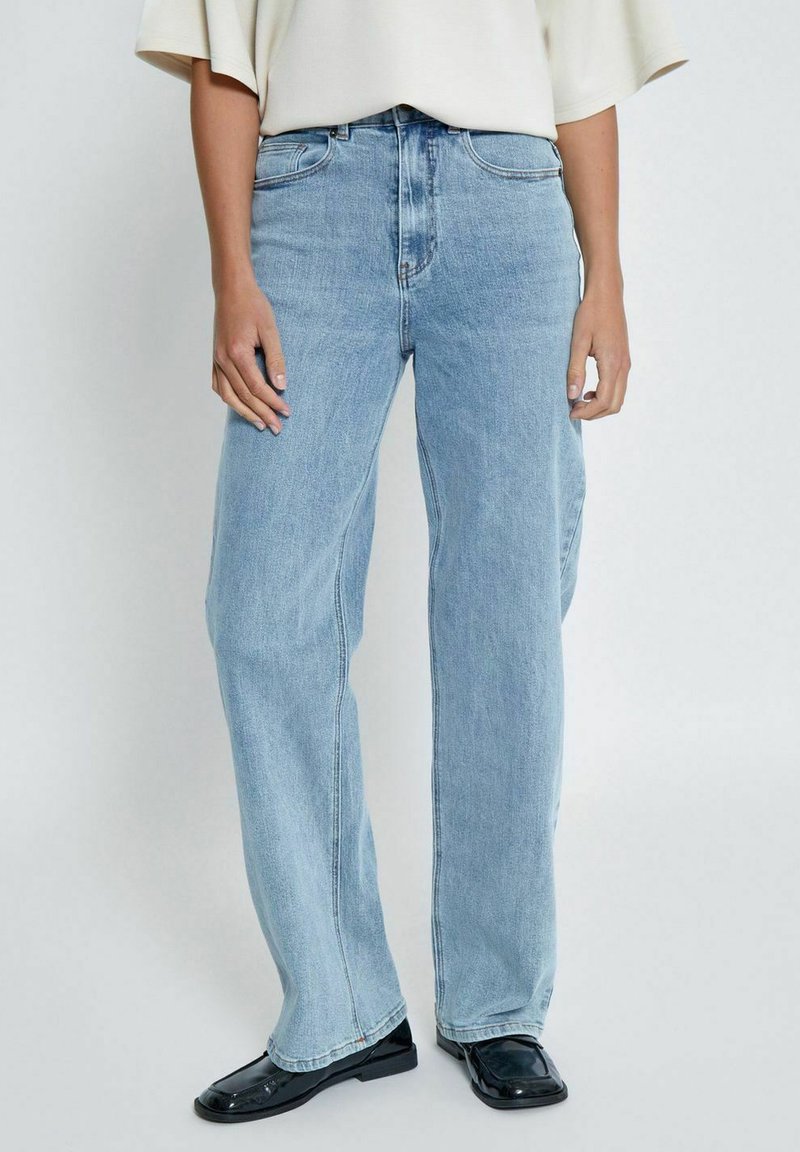 Heledad sinised, laiad teksad denim kangast, kõrge vöökohaga ja klassikalise viie taskuga disainiga. Kandmiseks mustade jalatsitega.
