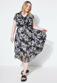 Mustapohjainen maksi mekko, jossa on violetteja ja vihreitä kuvioita, kevyttä kangasta, V-pääntie ja kerroksittainen hameen muotoilu.