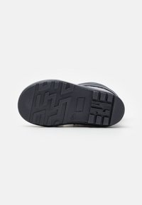 Suela de zapato de goma negra con un patrón de tracción texturizado, que presenta ranuras y elementos elevados para mayor agarre. Bordes de la superficie superior lisos.
