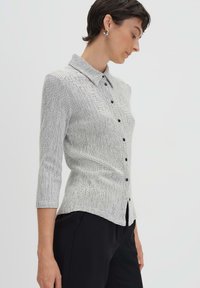 Camicia a maniche 3/4 a quadri bianchi e neri, con colletto e spacchi laterali, realizzata in un tessuto testurizzato.