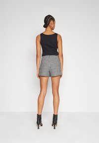 Black sleeveless top paired with high-waisted checkered shorts. The model also wears black heeled ankle boots, viewed from the back.