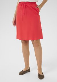 Red, knee-length skirt made of smooth, lightweight fabric. Features an elastic waistband with a drawstring and side pockets.