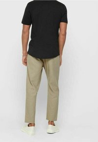 Schwarzes kurzärmeliges Hemd kombiniert mit hellbeigen, gerade geschnittenen Hosen und weißen Sneakern. Minimalistisches Design, Baumwollmaterial, lockere Passform.