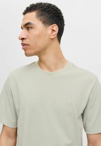 Tricou scurt cu manecă scurtă, de culoare verde deschis, fabricat dintr-un material moale, având un guler rotund și un logo mic pe piept. Textură netedă.