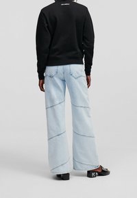 Czarna bluza, jasnoniebieskie spodnie o szerokich nogawkach z ukośnymi szwami oraz czarne sandały na platformie z akcentem logo. Tekstura jest miękka i swobodna.