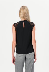 Top nera senza maniche con dettagli in pizzo sulle spalle e scollatura a chiave sul retro. Tessuto morbido, vestibilità comoda, abbinato a pantaloni grigi.