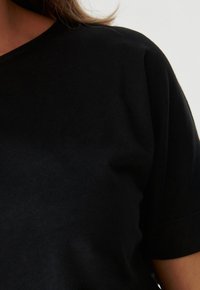 Černé tričko s kulatým výstřihem a krátkými rukávy, vyrobené z jemné hladké tkaniny s mírným leskem. Minimalistický design.