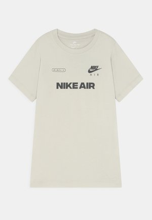 Jasnobeżowa koszulka z krótkim rękawem z czarnym napisem "NIKE AIR" oraz logo na środku przodu i na górze klatki piersiowej.