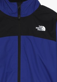 Giacca con zip blu e nera realizzata in tessuto resistente, presenta il logo The North Face in bianco, con cappuccio e design a pannelli contrastanti.