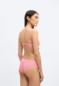 Rózsaszín csipkés melltartó és hozzáillő alsónemű geometriai mintával. A melltartón állítható vállpántok és kapcsos záródás található. Hátsó nézet sima textúrát mutat.