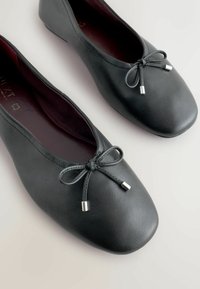 Zwarte leren ballerina's met een afgeronde neus, voorzien van een decoratieve strik met zilveren accenten. Soepele textuur en een gevoerde binnenkant.