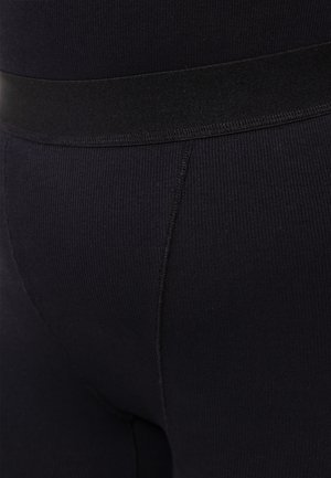 Schwarze gerippte Leggings mit einem weichen elastischen Bund und einem enganliegenden Design, das eine glatte und dehnbare Stofftextur betont.