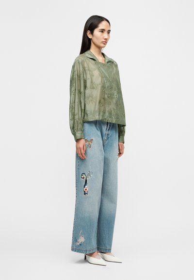 Διάφανη, ανοιχτό πράσινη μπλούζα με μακριά μανίκια και λουλουδένια σχέδια, συνδυασμένη με ανοιχτό μπλε τζιν παντελόνι με φαρδιές παντελόνες, διακοσμημένο με διάφορα κεντημένα σχέδια. Άσπρα μυτερά τακούνια.