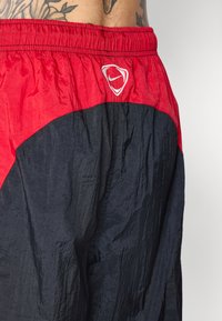 Shorts de sport Nike noirs et rouges portés par une personne tatouée, montrant la ceinture élastique et la texture du tissu en gros plan.