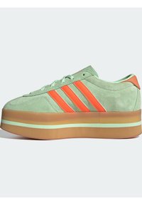 Zelené semišové tenisky se třemi oranžovými pruhy, silnou platformovou podrážkou se svěže zeleným akcentem a zaobleným designem špičky.