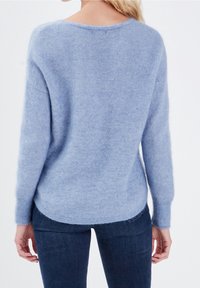 Jasnoniebieski dziergany sweter z długimi rękawami, okrągłym dekoltem i miękką, puszystą fakturą. Nieco dłuższy tył. Połączony z ciemnymi jeansami.