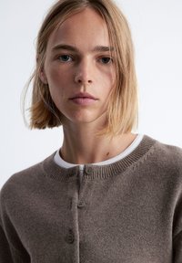 Hellbrauner Cardigan mit Rundhals, Knopfverschluss und geripptem Kragen. Er besitzt eine weiche Textur und ein einfaches, klassisches Design.