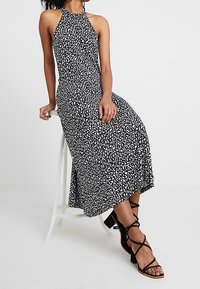 Black and white patterned halter neck dress with a fitted bodice and flowing skirt, paired with strappy black high heels.