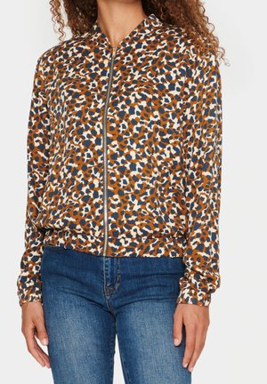 Donna che indossa una giacca con zip di un motivo astratto a leopardo nei colori marrone, blu navy e bianco, abbinata a jeans blu.
