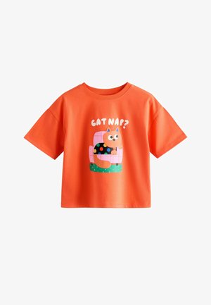 Cămașă portocalie cu mâneci scurte, cu o pisică desen animat care poartă un pulover negru cu buline, stând pe un scaun roz, și textul „CAT NAP?” deasupra.