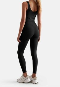Top atletico nero e leggings realizzati con materiale elastico, caratterizzati da un design aderente. Abbinamento con scarpe sportive bianche come calzature.